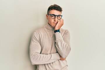 Hispanic young man wearing casual turtleneck sweater thinking looking tired and bored with depression problems with crossed arms.