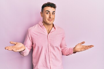 Hispanic young man wearing casual clothes clueless and confused expression with arms and hands...