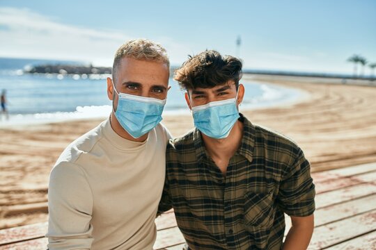 Young gay couple wearing medical mask sitting on the bench at the beach.