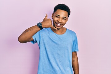 Young african american man wearing casual blue t shirt smiling doing phone gesture with hand and fingers like talking on the telephone. communicating concepts.