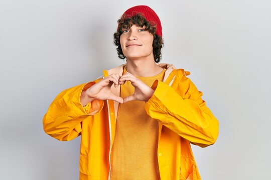 Handsome young man wearing yellow raincoat smiling in love showing heart symbol and shape with hands. romantic concept.