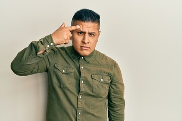 Young latin man wearing casual clothes pointing unhappy to pimple on forehead, ugly infection of...