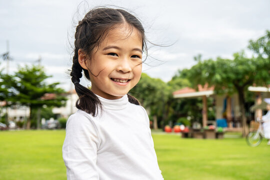Portrait of Cute asian little girl standing in summer park looking in camera smiling happily, Laughing child, Expressive facial expressions.