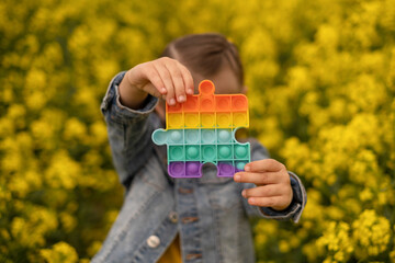 A child holds a popular toy popit rapeseed field. Useful toys for the development of fine motor...