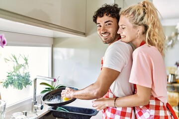 Obraz premium Young couple smiling happy and hugging washing dishes at kitchen.