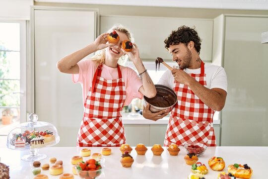 Young couple smiling happy cooking sweets holding pumpkin on eyes at kitchen.