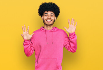 Young african american man with afro hair wearing casual pink sweatshirt showing and pointing up with fingers number nine while smiling confident and happy.