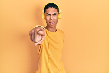 Young african american guy listening to music using headphones pointing displeased and frustrated to the camera, angry and furious with you