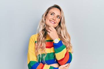 Beautiful young blonde woman wearing colored sweater with hand on chin thinking about question, pensive expression. smiling and thoughtful face. doubt concept.