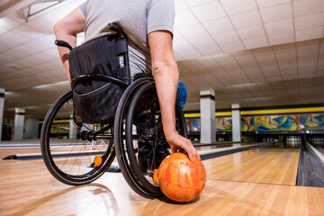 Young disabled man in wheelchair playing bowling in the club