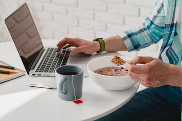 handsome smiling man in shirt sitting in kitchen at home at table working online on laptop