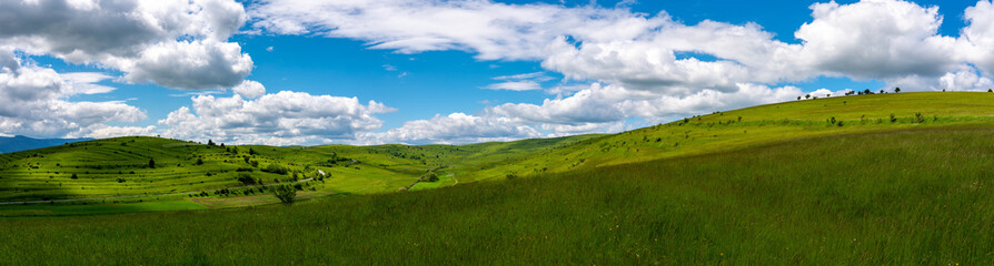 Fototapeta premium Panoramic scenic view of green hills at springtime, blue sky with white clouds in Transylvania, Romania.