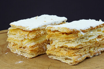 Puff pastry cakes with powdered sugar and cream on wooden board. Selective focus.