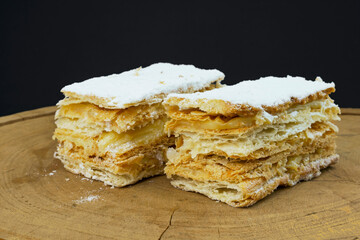 Puff pastry cakes with powdered sugar and cream on wooden board. Selective focus.