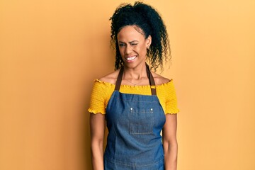 Middle age african american woman wearing professional apron winking looking at the camera with sexy expression, cheerful and happy face.