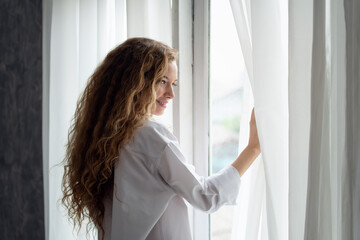 Young woman opening the curtain in the morning