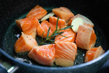 Salmon Belly or Salmon Toro sliced with rosemary and garlic cooking on pan.