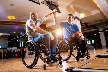 Obraz na płótnie Canvas Two young disabled men in wheelchairs playing bowling in the club