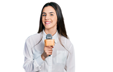 Young brunette teenager holding reporter microphone looking positive and happy standing and smiling...