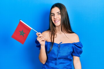 Young brunette teenager holding morocco flag looking positive and happy standing and smiling with a confident smile showing teeth