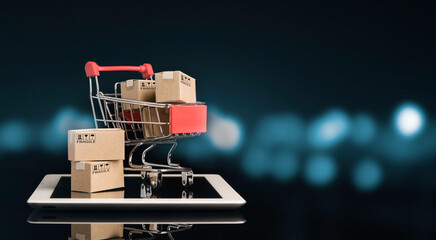 Shipping paper boxes inside Red shopping cart trolley on tablet with black and blue bokeh...