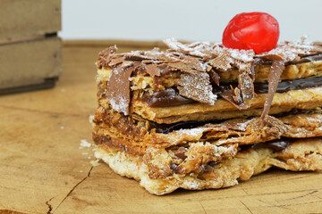 Puff pastry cakes with powdered sugar and chocolate cream on wooden board. Close up and selective focus.