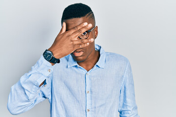 Young african american man wearing casual clothes and glasses peeking in shock covering face and eyes with hand, looking through fingers afraid