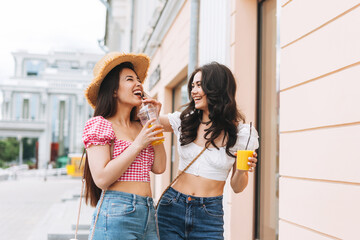 Happy smiling beautiful brunette young women friends in summer clothes with juice in hands walking...