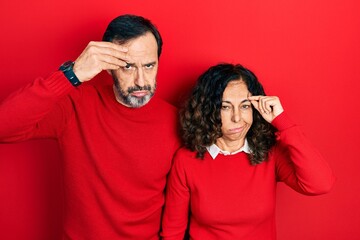 Middle age couple of hispanic woman and man hugging and standing together worried and stressed about a problem with hand on forehead, nervous and anxious for crisis