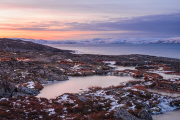 Wonderful mountain landscape with a cape on the shore of the Barents sea. Amazing sunrise landscape with polar white snowy range of mountains.