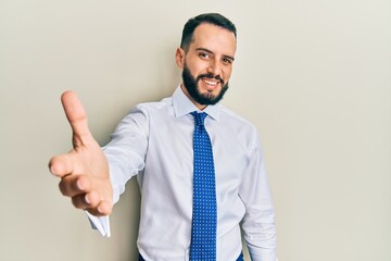 Young man with beard wearing business tie smiling friendly offering handshake as greeting and welcoming. successful business.