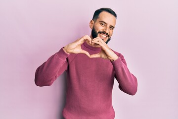 Obraz premium Young man with beard wearing casual winter sweater smiling in love doing heart symbol shape with hands. romantic concept.