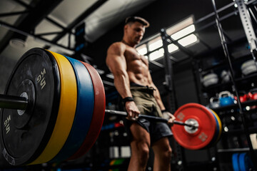 Fototapeta Weightlifting and the concept of sports life. A half-naked man stands in the middle of the gym and raises a barbell with weight plates. Dead lift with high load. Strength and energy, bodybuilding obraz