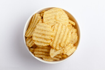 Close up of Wrinkled Wavy Potato Chips in white ceramic bowl, Popular Ready to eat crunchy, salty pale-yellow color over white background
