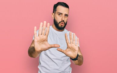 Young man with beard wearing casual white t shirt moving away hands palms showing refusal and...