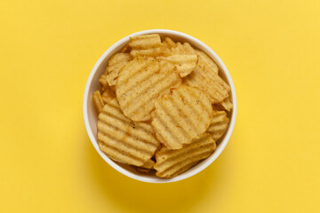 Close up of Wrinkled Wavy Potato Chips in white ceramic bowl, Popular Ready to eat crunchy, salty pale-yellow color over yellow background
