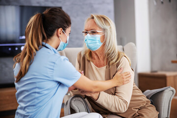 Nurse sitting at home with pensioner and comforting her during corona virus pandemic. They both have face masks.