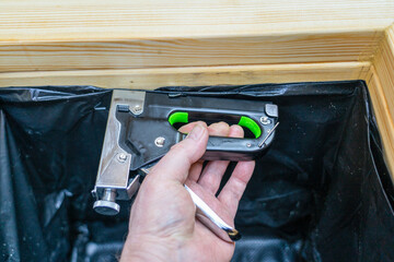 Man firing a industrial stapler gun to secure a planter black liner into lumber boards