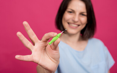 Beautiful happy young woman using interdental brush on the pink background