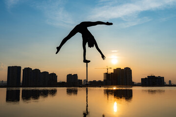 Flexible female circus Artist keep balance and touching the sun against dramatic sunset and...