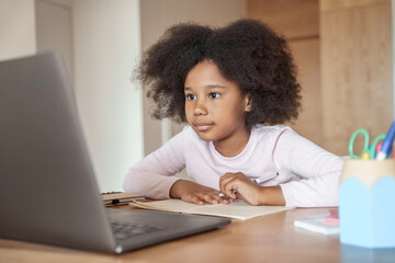 Little african american girl looking at laptop screen studying from home