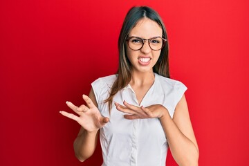 Young brunette woman wearing casual clothes and glasses disgusted expression, displeased and fearful doing disgust face because aversion reaction. with hands raised