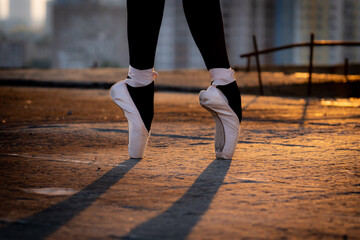 Fototapeta na wymiar Close up of a ballet dancer's feet in shoes in urban place during sunset. Concept of individuality, creativity and passion