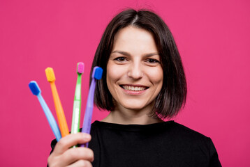 Beautiful happy young woman with different colored toothbrushes on blank pink background