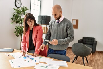 Two hispanic business workers with serious expression working using smartphone at the office.