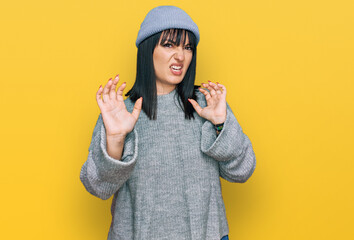 Young hispanic woman wearing cute wool cap afraid and terrified with fear expression stop gesture with hands, shouting in shock. panic concept.