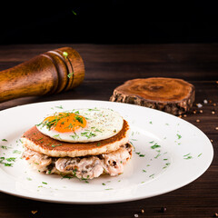 A stack of buckwheat pancakes with mushroom sauce and fried eggs on a wooden background. Tasty and healthy breakfast