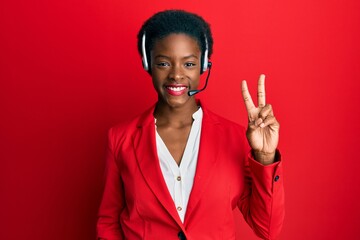 Young african american girl wearing call center agent headset smiling with happy face winking at...