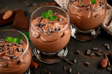 Vegan chocolate mousse with mint, bar of chocolate and cocoa beans on a dark background.