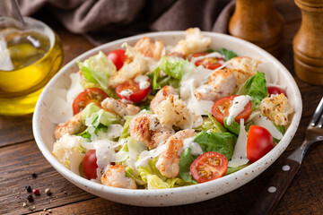 Salad with grilled chicken breast, romaine lettuce, tomatoes and sauce known as Caesar salad served on plate, wooden table background - obrazy, fototapety, plakaty